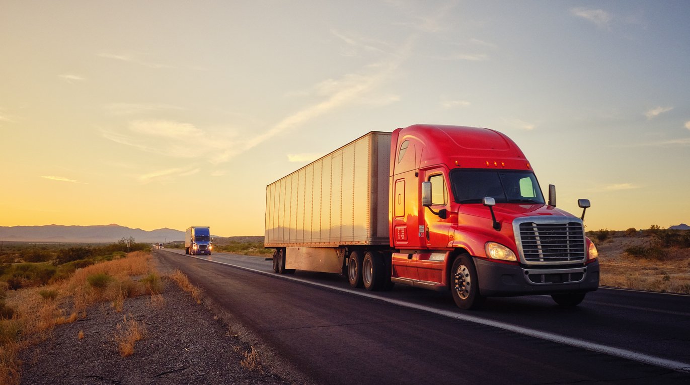Large semi truck hauling freight on the open highway in the western USA under an evening sky.