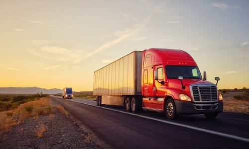 Large semi truck hauling freight on the open highway in the western USA under an evening sky.